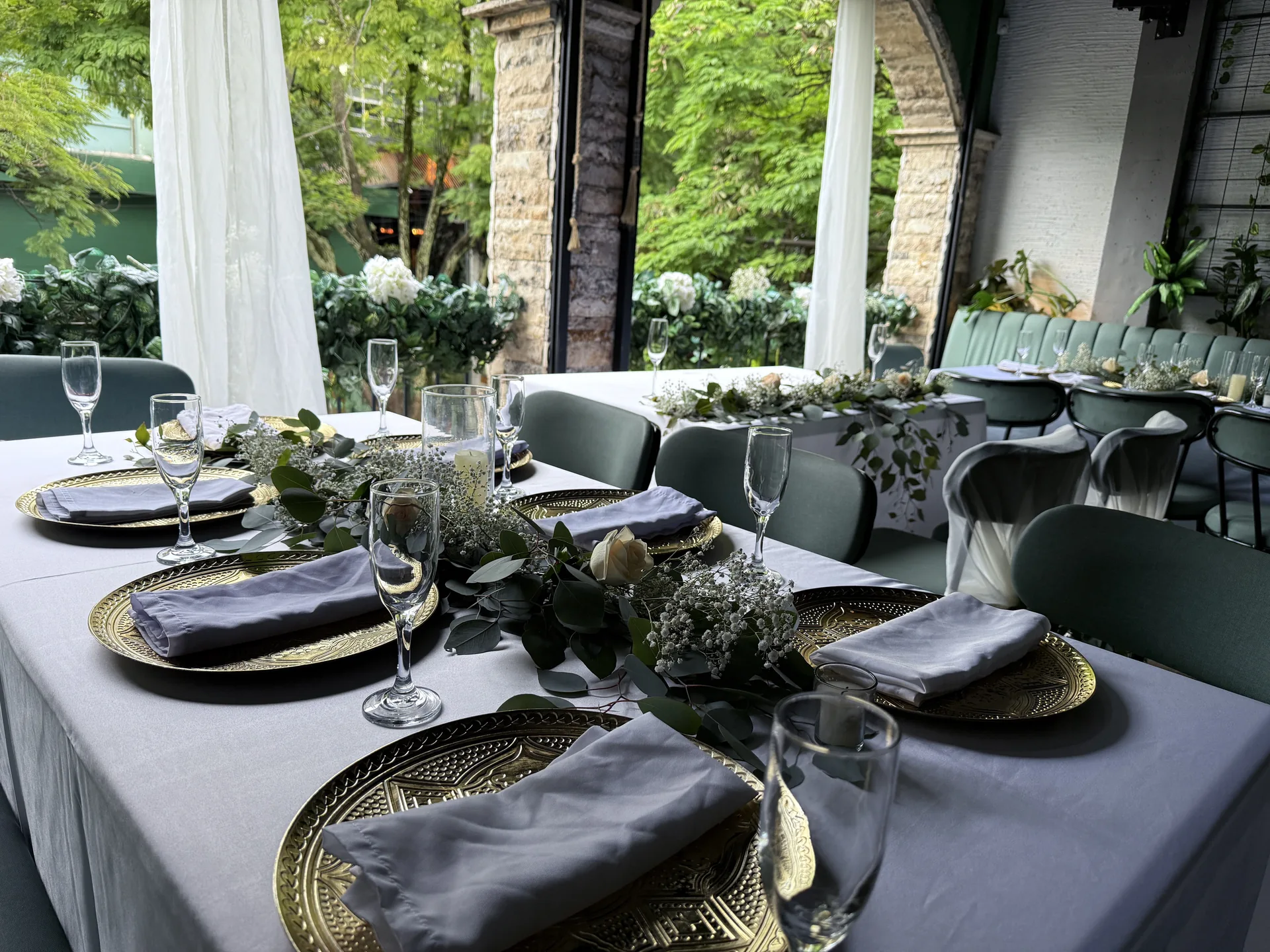 Mesa tendida con vajilla dorada, verdes y velas en el salón de Kampanas
